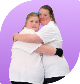 Two adult dancers are hugging eachother with both arms and heads together smiling and posing for their photo wearing their All Abilities Australia t-shirts